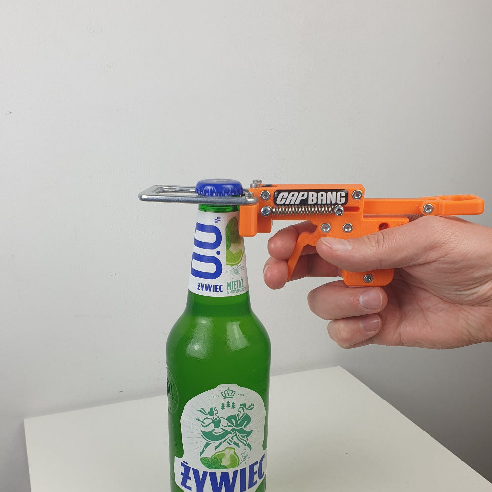 Person using a Cap Bang bottle opener on a Zywiec bottle against a white background