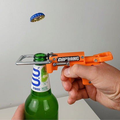 Person using an orange 'CapBang' bottle opener on a green bottle with a gray background