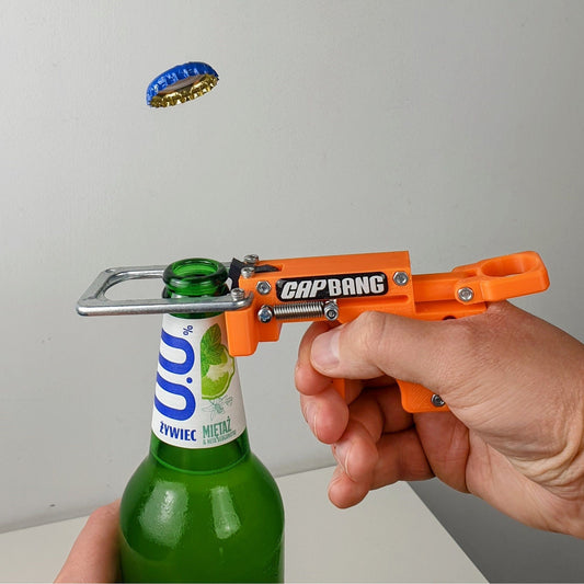 Person using an orange 'CapBang' bottle opener on a green bottle with a gray background